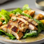 "A bowl of fresh chicken Caesar salad with grilled chicken, romaine lettuce, Parmesan cheese, and croutons on a wooden table."